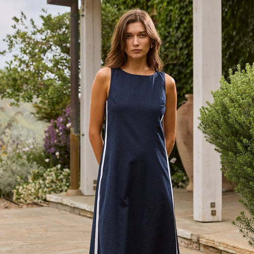 Woman wearing a navy dress with white stripes standing outdoors near plants and flowers.