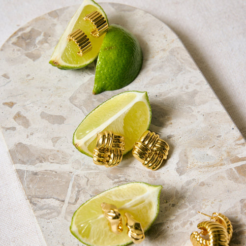 Gold earrings on a marble surface with lime wedges