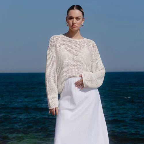 Woman in a white outfit standing on a rocky shore with ocean in the background