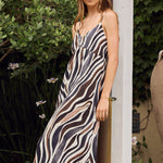 Woman in a zebra-striped dress standing outdoors near a wooden post.