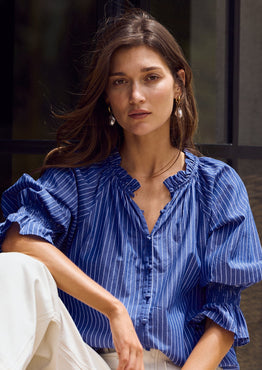 Woman wearing a blue shirt and white pants sitting on steps.
