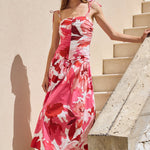 Woman in a pink floral dress walking up stone steps against a beige wall.