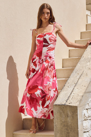 Woman in a pink floral dress walking up stone steps against a beige wall.