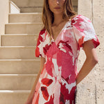 Woman in a red and white floral dress standing on stone steps outdoors.