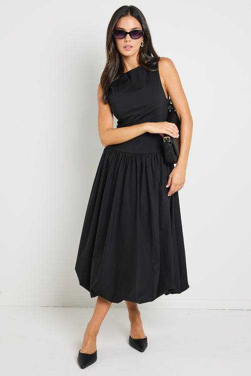 Woman wearing a black bubble hem midi dress, styled with black flats for a playful yet sophisticated look.