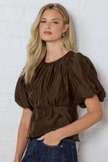 Woman wearing a brown blouse against a white brick wall