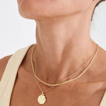 Close-up of a person wearing a gold necklace with a coin pendant on a plain background