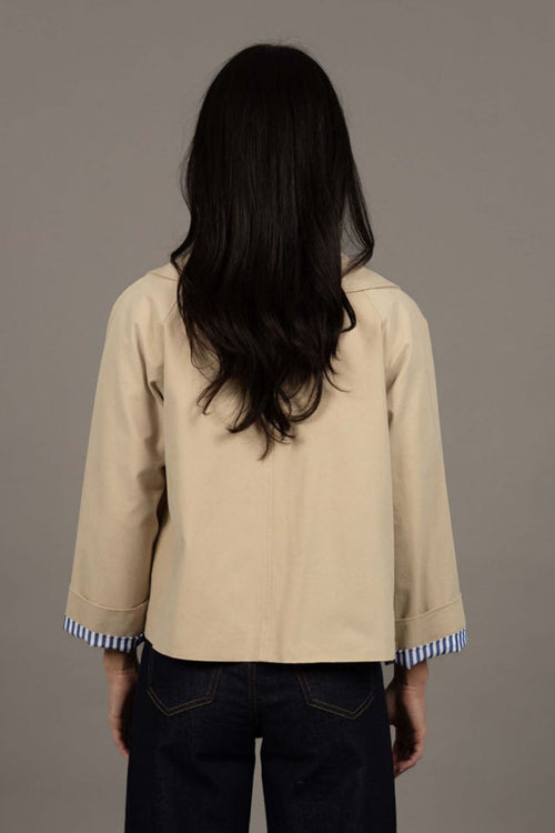 Person wearing a beige jacket with blue trim on a plain background