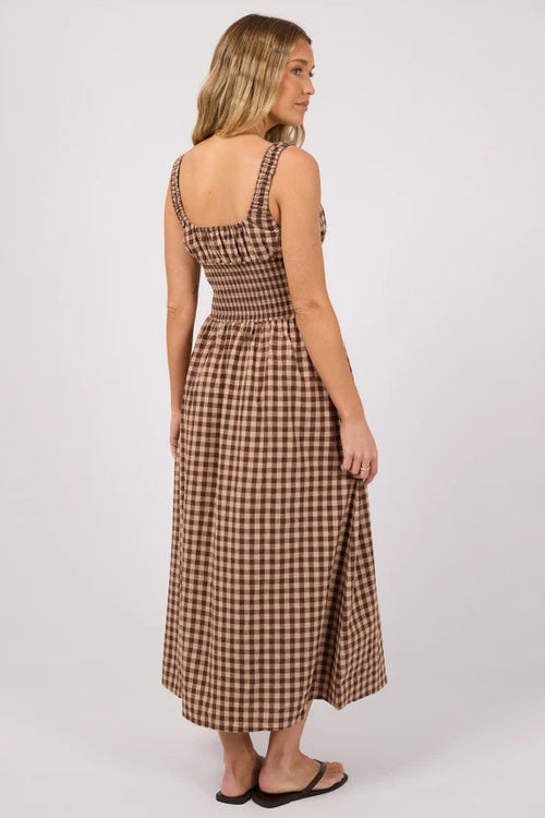 A woman modeling a brown and beige gingham midi dress from the back, standing against a plain light gray studio background.