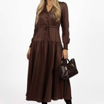 Woman wearing a brown dress holding a matching handbag on a white background