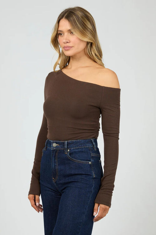Woman wearing a brown off-shoulder top and blue jeans on a white background