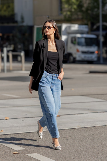 Woman walking on a city street wearing a black blazer, black top, and light blue jeans.