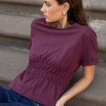 Woman wearing a purple top and blue jeans sitting on steps.