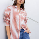 Woman wearing a red and white striped shirt and blue jeans against a white wall.