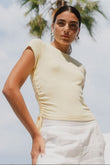 Woman wearing a light-colored top and white pants with palm trees in the background