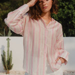 Woman wearing a pink and white striped shirt with a blurred outdoor background