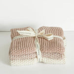 Two folded chunky-knit baby blankets in dusty pink and cream, tied together with a cream ribbon printed with the brand name 'bianco foraggio'.