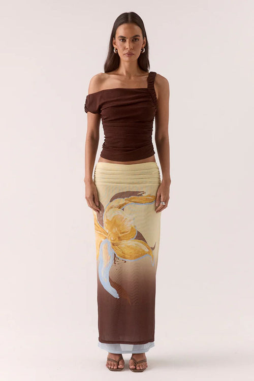 Woman wearing a brown off-shoulder top and a long, patterned skirt on a white background