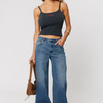 Woman wearing a black tank top and blue jeans holding a brown bag on a white background