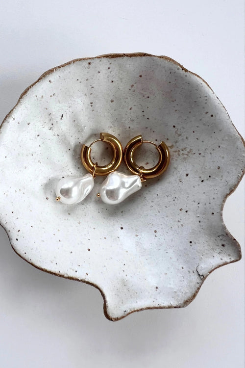 A pair of gold-toned hoop earrings featuring dangling baroque freshwater pearls, suspended from smooth, polished hoops for an elegant and organic look