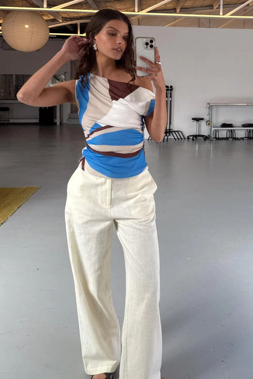 Woman taking a mirror selfie wearing a colorful top and white pants in an indoor setting.