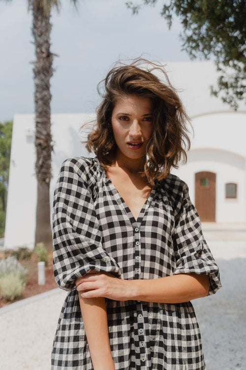 Woman wearing a black and white gingham mini dress with a button-down front, tiered skirt, and mid-length sleeves.