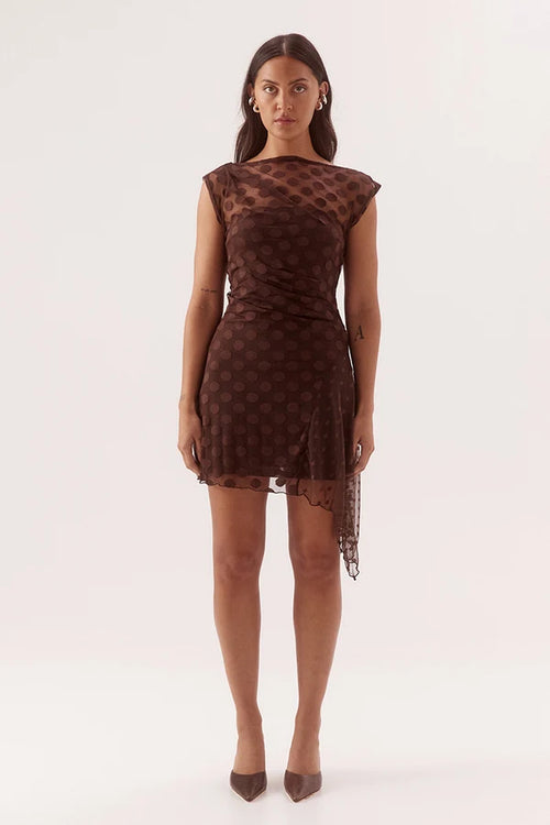 A woman modeling a brown sheer mesh mini dress with a dark brown polka dot pattern, photographed against a seamless white studio background.