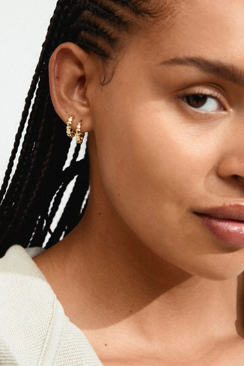 Close-up of a woman's ear with gold earrings against a neutral background