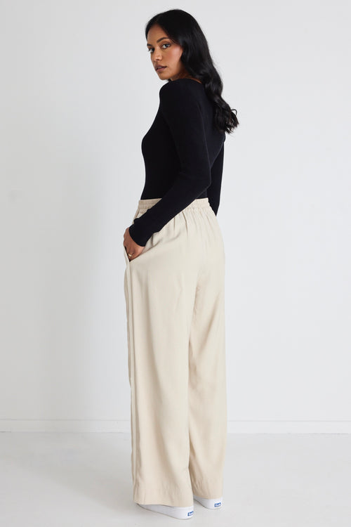 Model wears black long sleeve top with beige pants