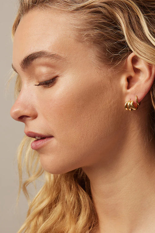 Close-up of a woman wearing gold hoop earrings with a neutral background