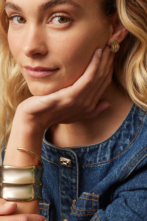 Woman wearing a denim jacket and gold jewelry against a neutral background
