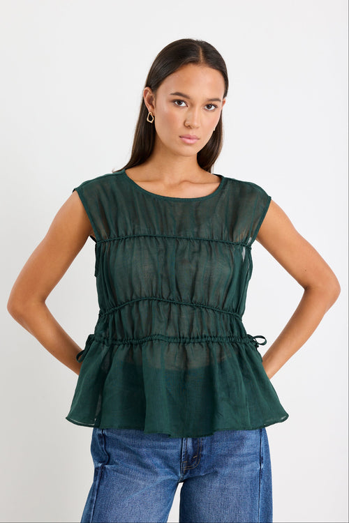 Woman wearing a green peplum top and blue jeans on a white background