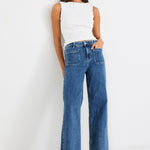 Woman wearing a white sleeveless top and blue jeans on a white background