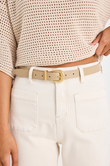 Person wearing a beige sweater and white pants with a beige belt.
