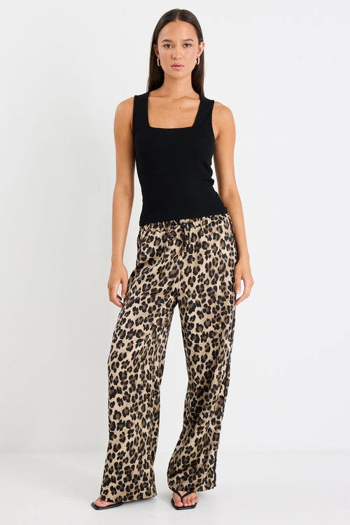 Woman wearing a black sleeveless top and leopard print pants on a white background