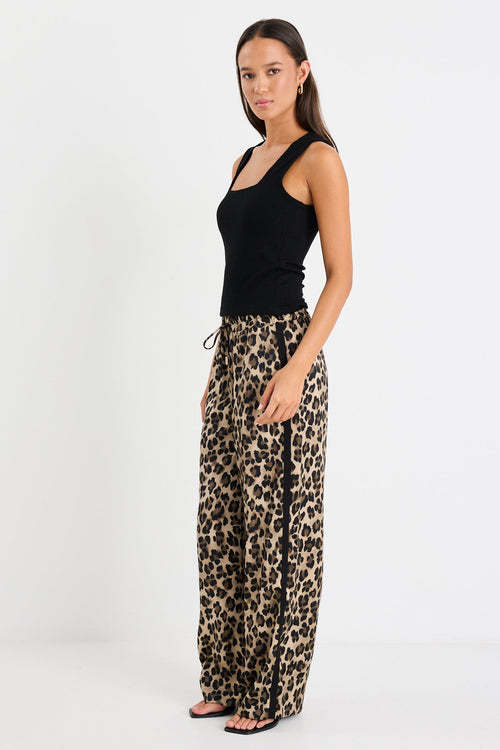 Woman wearing a black top and leopard print pants on a white background