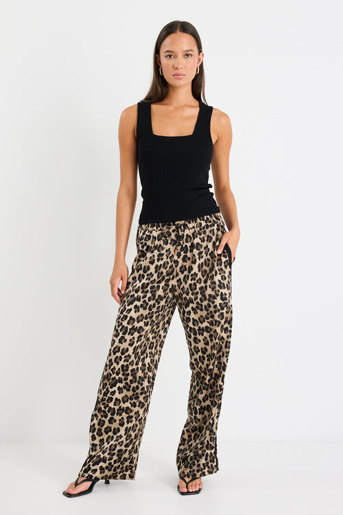 Woman wearing a black sleeveless top and leopard print pants on a white background