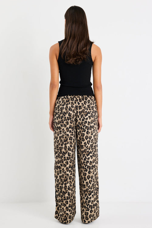 Woman wearing leopard print pants and a black top on a white background