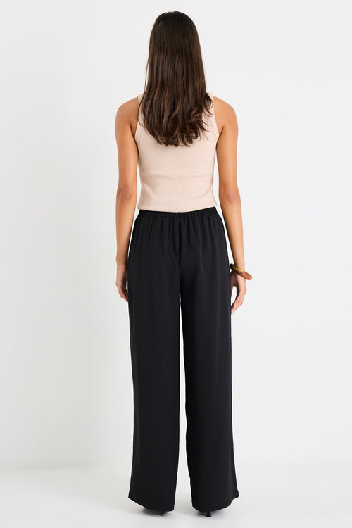 Woman wearing a beige sleeveless top and black wide-leg pants on a white background