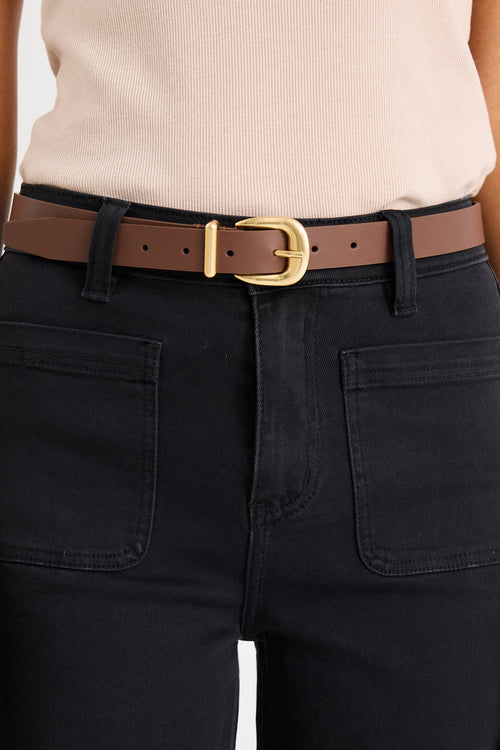 Person wearing black pants with a brown belt and beige top on a white background
