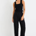 Woman wearing a black sleeveless top and wide-leg pants with white stripes on a white background