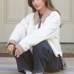 Woman sitting on steps wearing a white coat and dark jeans.