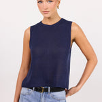A woman modeling a sleeveless navy blue knit top with light-wash blue jeans and a black belt, standing against a plain light background.