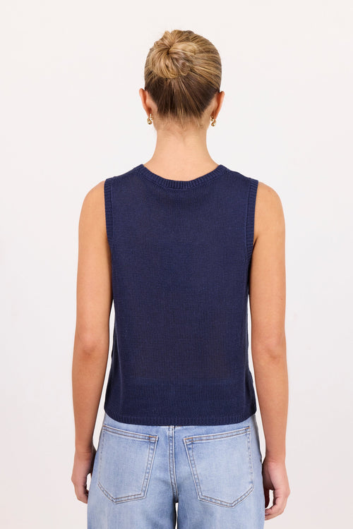 A woman viewed from the back wearing a sleeveless navy blue top and light blue jeans against a plain white background.