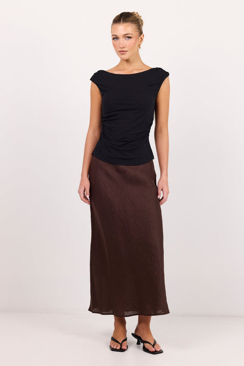 A woman modeling a black short-sleeve top and a dark brown midi skirt against a plain white studio background.