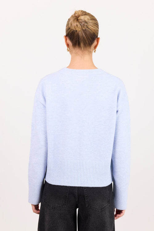 A person viewed from the back wearing a light periwinkle blue knit sweater and dark wide-leg jeans against a plain off-white background.