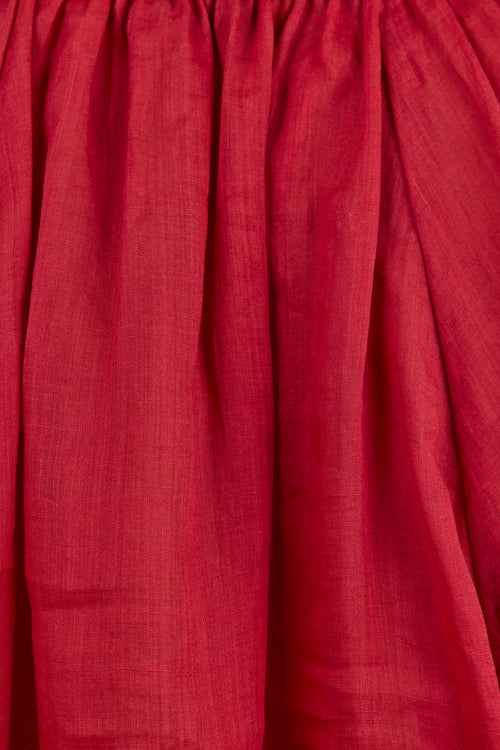 A close-up of a deep red or burgundy pleated fabric, showing the texture and folds of the material.