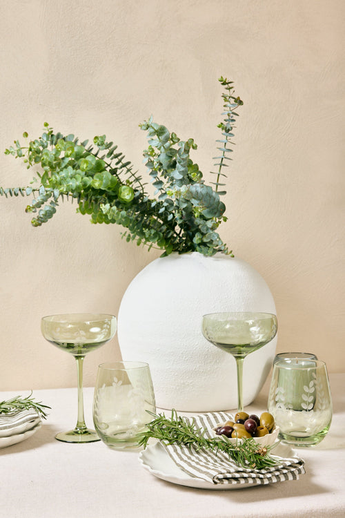 Table setting with greenery, glasses, and plates on a beige background