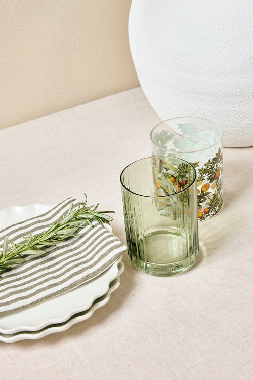 Table setting with green glassware, white plates, and floral arrangements on a neutral background