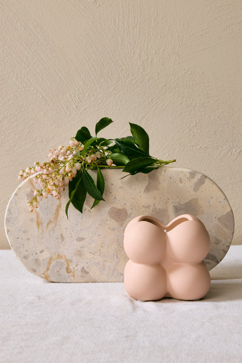 Decorative vase with a marble base and a small pink ceramic piece on a neutral background